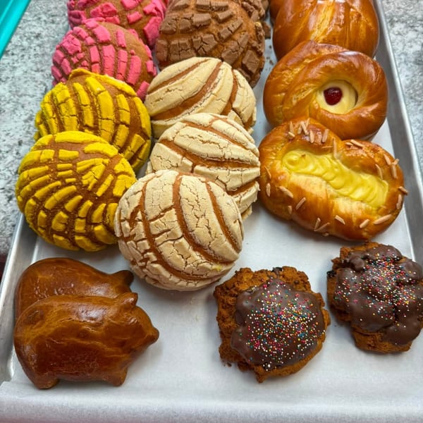 A tray filled with colorful Mexican conchas, sweet breads, pig-shaped pastries, and chocolate cookies.