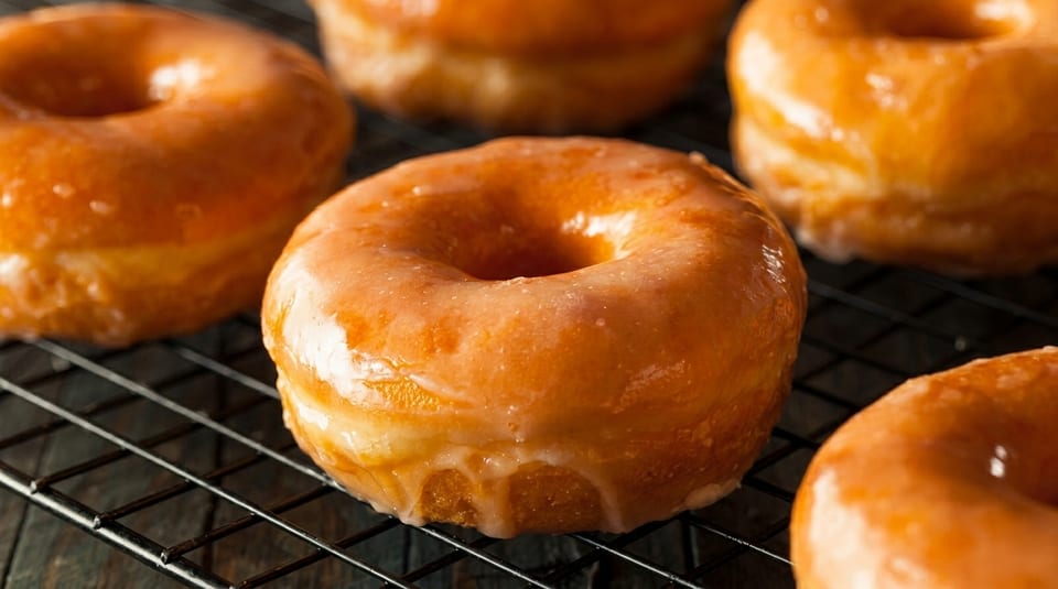Several golden-brown glazed donuts are cooling on a black wire rack, with a dark wooden surface below.