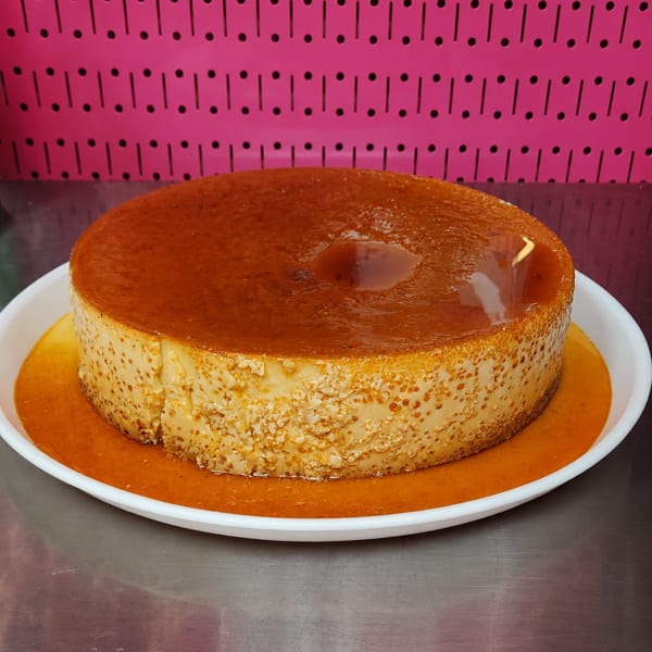 Large caramel flan on a white plate with a pink pegboard background.