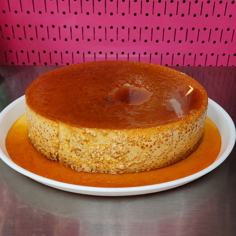 Large caramel flan on a white plate with a pink pegboard background.