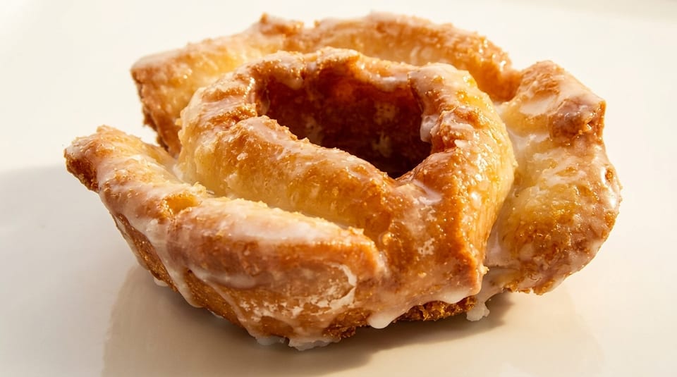 Close-up of a glazed old-fashioned donut with a golden-brown, crinkled texture on a white surface.