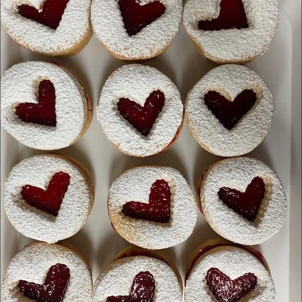 Heart-shaped jam cookies with powdered sugar arranged neatly in rows.